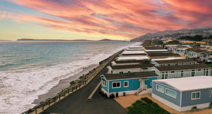 Coastal mobile homes along a beachfront road at sunset, with waves and a dramatic sky overhead in Pacifica, CA