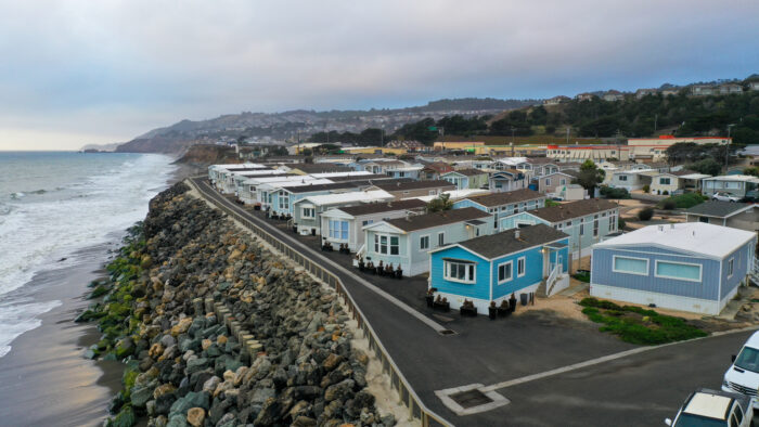 Aerial view of coastal mobile homes along a rocky shoreline under a cloudy sky in Pacifica, CA