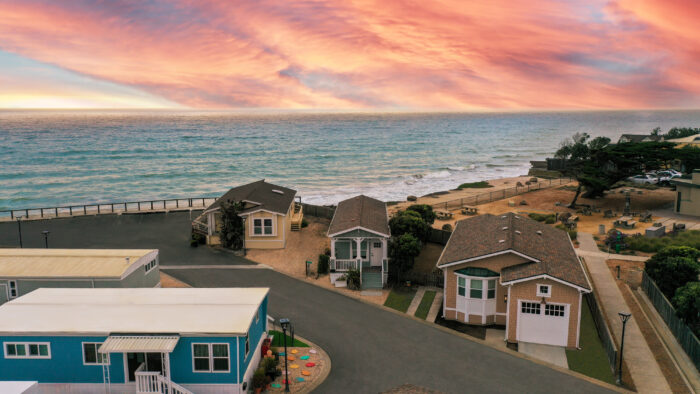 Aerial view of coastal homes near the ocean, with a vibrant sunset sky and community spaces visible by the shoreline in Pacifica, CA