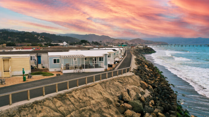 Oceanfront mobile homes on a bluff with a paved road and a dramatic pink and orange sunset sky in Pacifica, CA