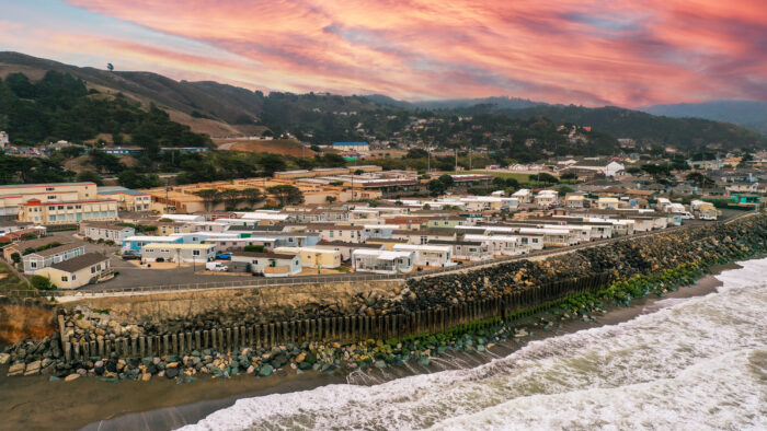 Wide view of a mobile home park on the coastline, with ocean waves and a vibrant pink sunset sky in Pacifica, CA
