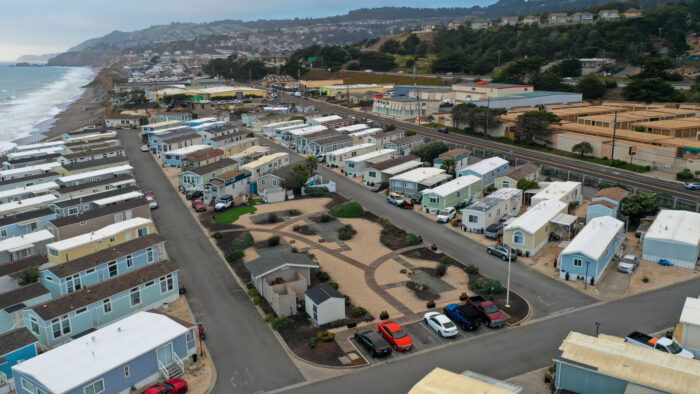 Aerial view of a coastal mobile home community with landscaped common areas and roads near a highway in Pacifica, CA