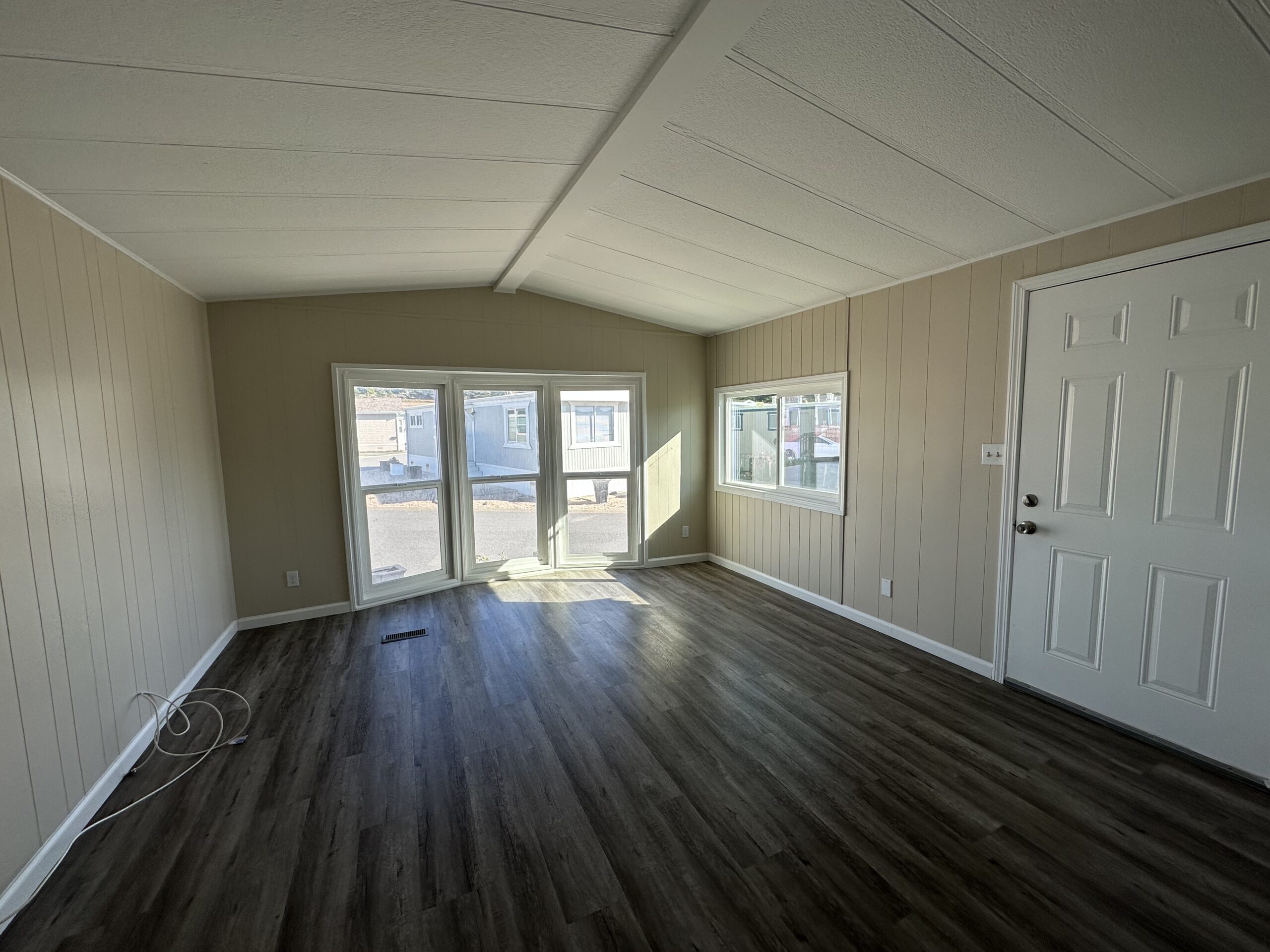 Spacious room with natural light, featuring beige walls, dark flooring, and a white door.