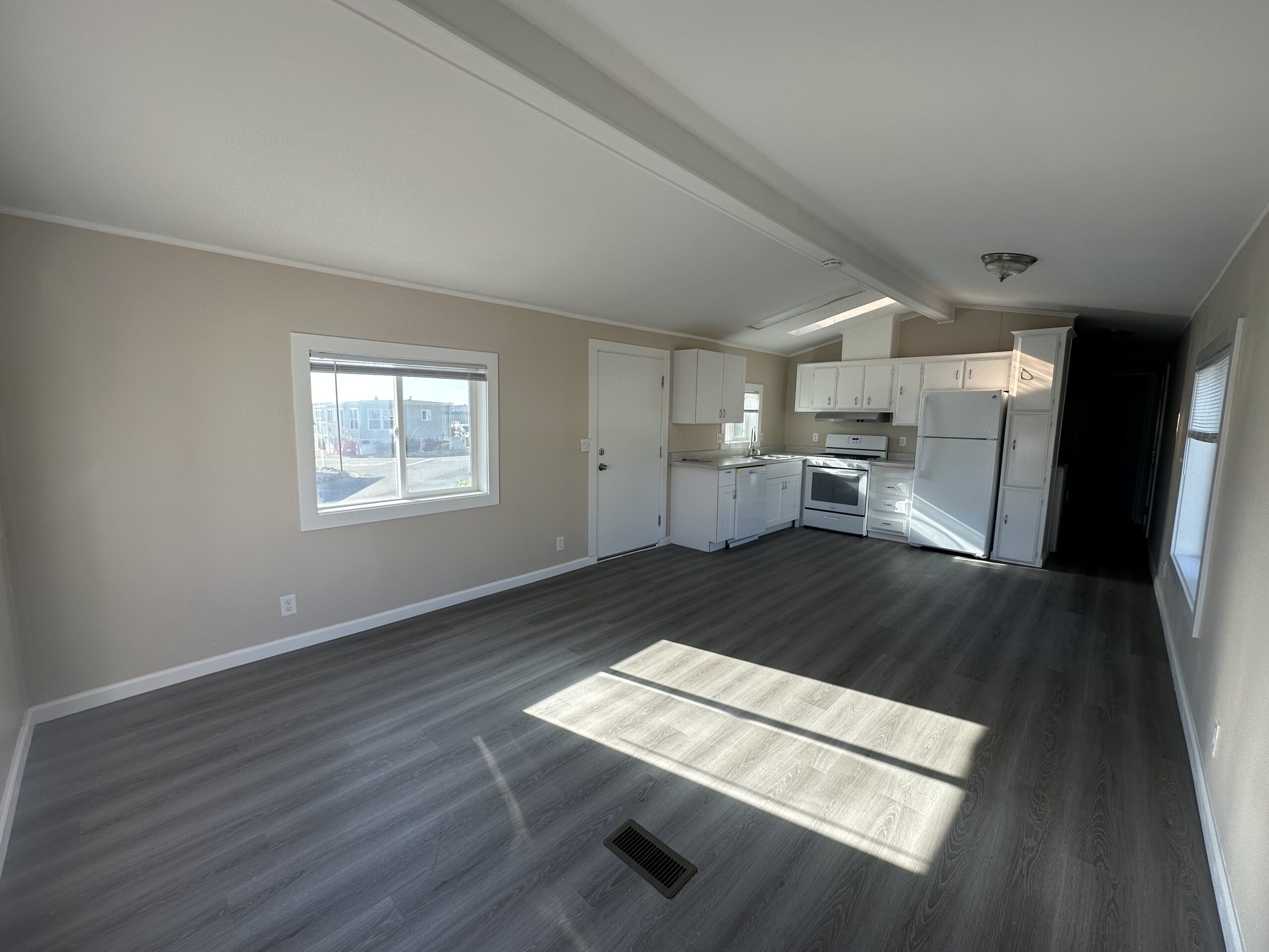 Sunlit open-plan living space with kitchen, featuring white appliances and dark wood flooring.