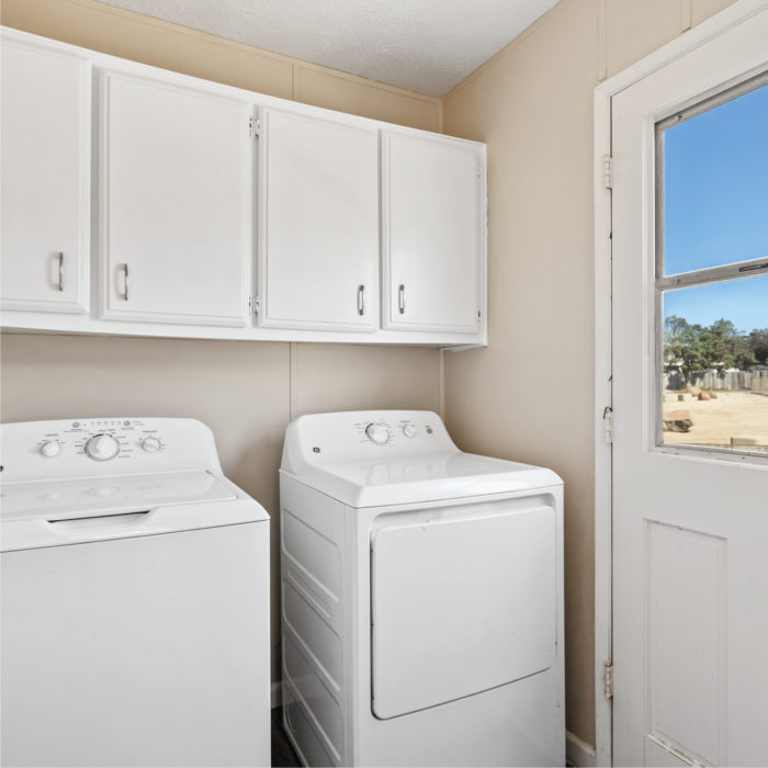 The laundry room inside a manufactured home features a washing and drying machines under white wood cabinets.