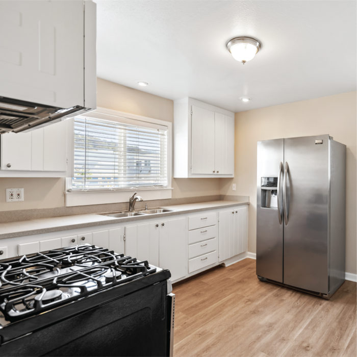 Kitchen with laminate floors feature white wood cabinets and a modern steeltall fridge.