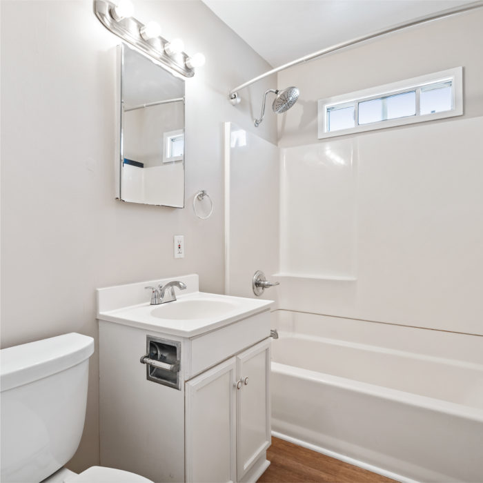 A white clean bathroom with nice shower and vanity mirror.