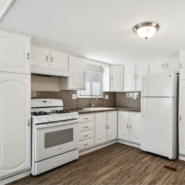Modern kitchen inside a manufactured home features white wood cabinets and steel appliances.